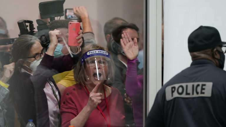 Election challengers yell as they look through the windows of the central counting board as police were helping to keep additional challengers from entering due to overcrowding, Wednesday, Nov. 4, 2020, in Detroit. (AP Photo/Carlos Osorio)